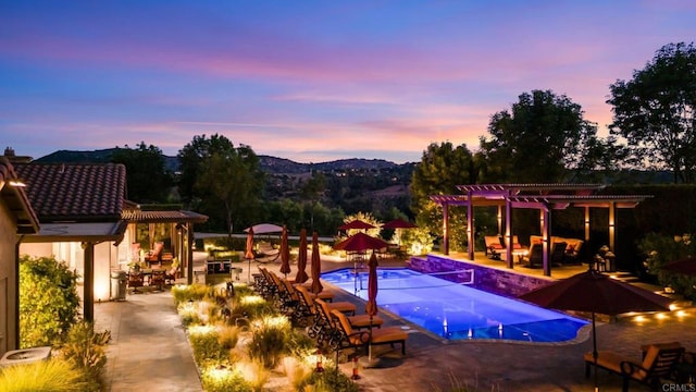 pool at dusk with a mountain view, a patio area, and a pergola