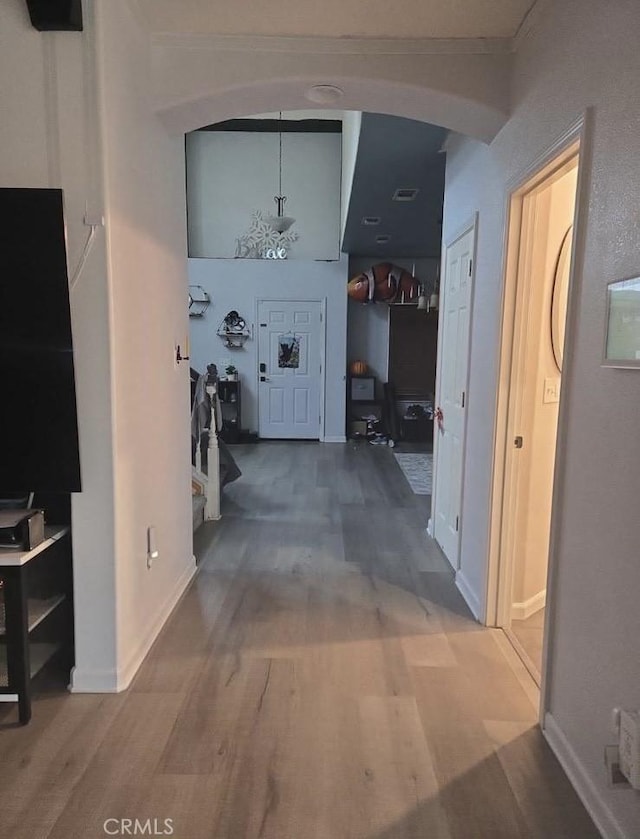 hallway featuring arched walkways, wood finished floors, visible vents, and baseboards