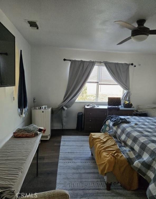 bedroom featuring dark wood-type flooring, visible vents, ceiling fan, and a textured ceiling