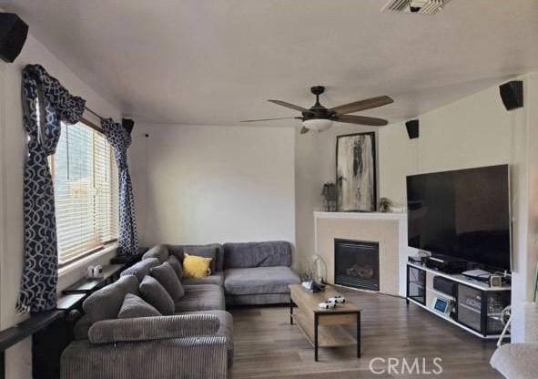 living area with ceiling fan, visible vents, wood finished floors, and a glass covered fireplace