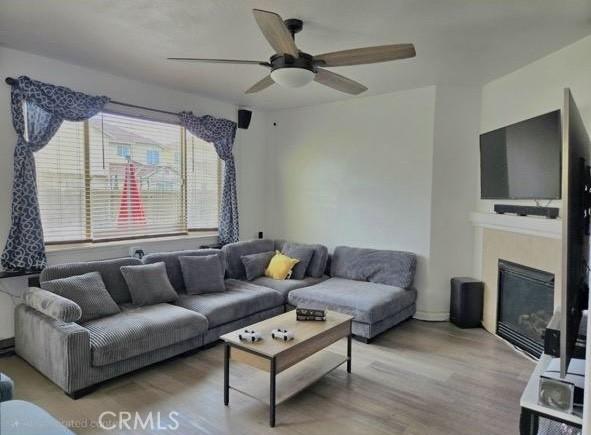 living room with ceiling fan, light wood finished floors, and a glass covered fireplace