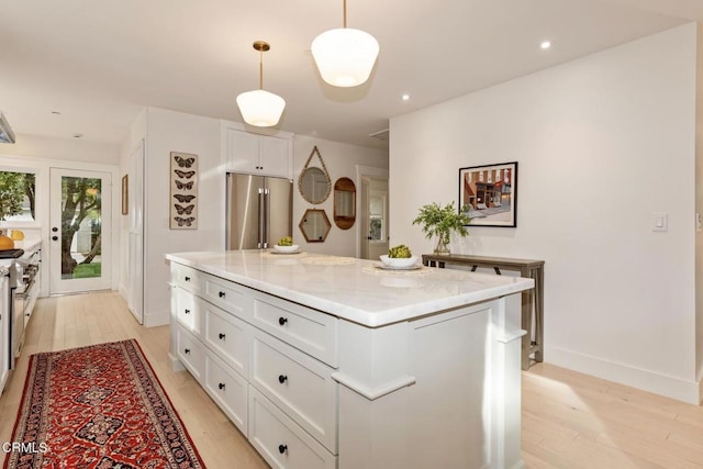 kitchen with a kitchen island, high quality fridge, decorative light fixtures, white cabinets, and light stone countertops