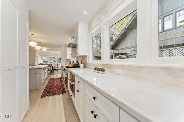 kitchen featuring appliances with stainless steel finishes, white cabinets, backsplash, light stone counters, and light wood-type flooring