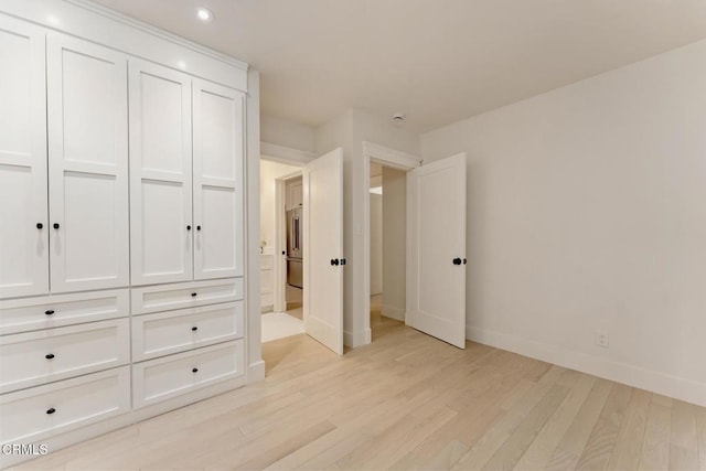 unfurnished bedroom with high end refrigerator, a closet, and light wood-type flooring