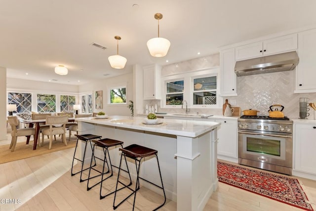 kitchen featuring decorative light fixtures, high end stove, white cabinetry, decorative backsplash, and a center island