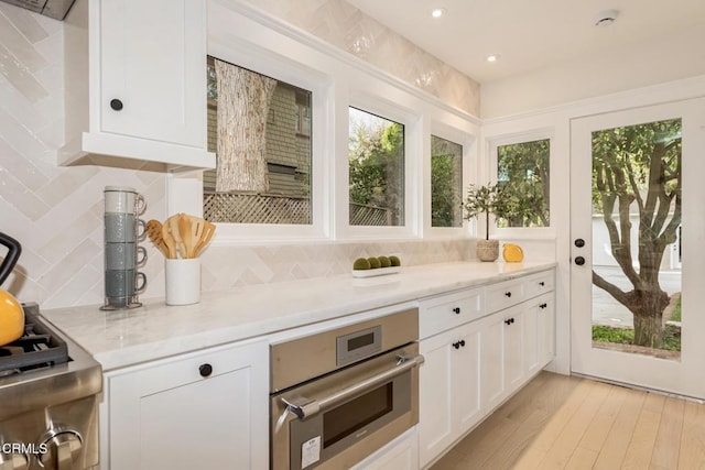 kitchen featuring white cabinetry, decorative backsplash, light stone countertops, and oven