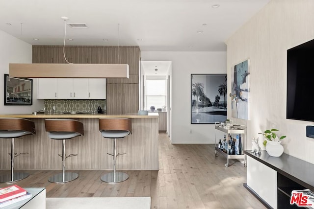 kitchen with light wood-type flooring, a kitchen breakfast bar, kitchen peninsula, white cabinets, and backsplash