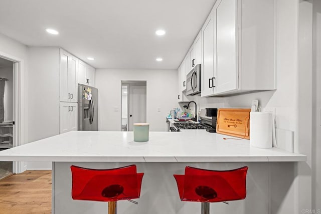 kitchen featuring white cabinetry, stainless steel appliances, kitchen peninsula, and a breakfast bar