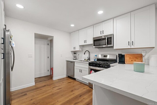 kitchen featuring sink, stainless steel appliances, light stone counters, white cabinets, and light wood-type flooring