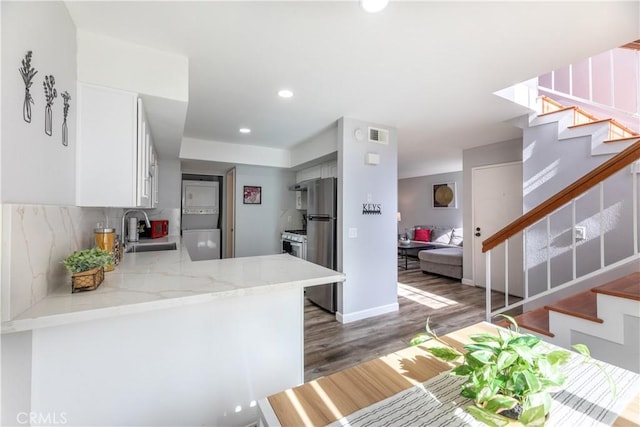 kitchen featuring stacked washer and clothes dryer, sink, white cabinetry, kitchen peninsula, and backsplash