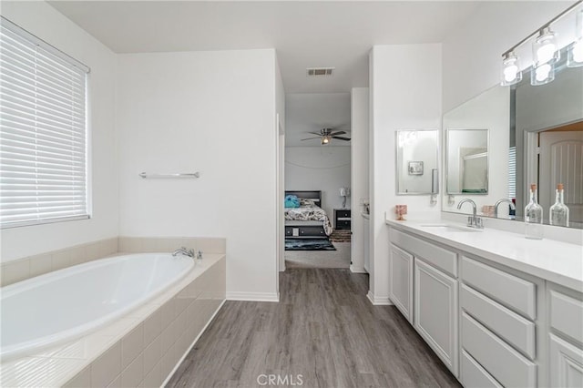 bathroom with vanity, hardwood / wood-style floors, ceiling fan, and tiled tub