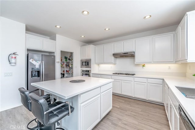 kitchen with a center island, appliances with stainless steel finishes, a kitchen breakfast bar, light hardwood / wood-style floors, and white cabinets