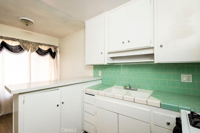 kitchen featuring tile countertops, white cabinetry, decorative backsplash, gas range oven, and a textured ceiling