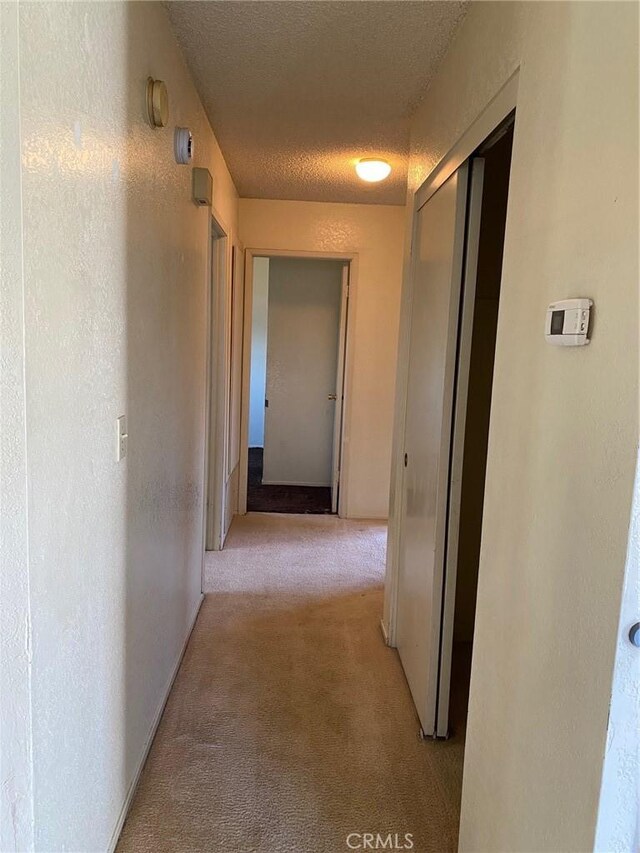 hallway featuring light colored carpet and a textured ceiling