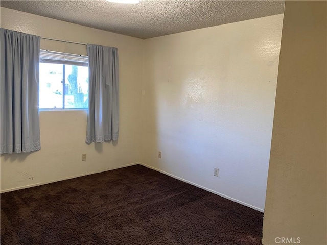 spare room featuring dark colored carpet and a textured ceiling