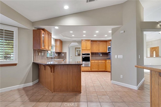 kitchen with light tile patterned floors, decorative backsplash, kitchen peninsula, and appliances with stainless steel finishes