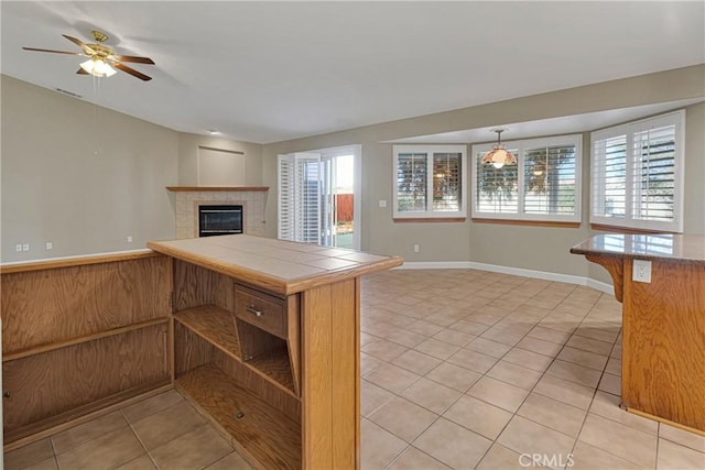 kitchen featuring a tile fireplace, tile countertops, hanging light fixtures, light tile patterned floors, and ceiling fan