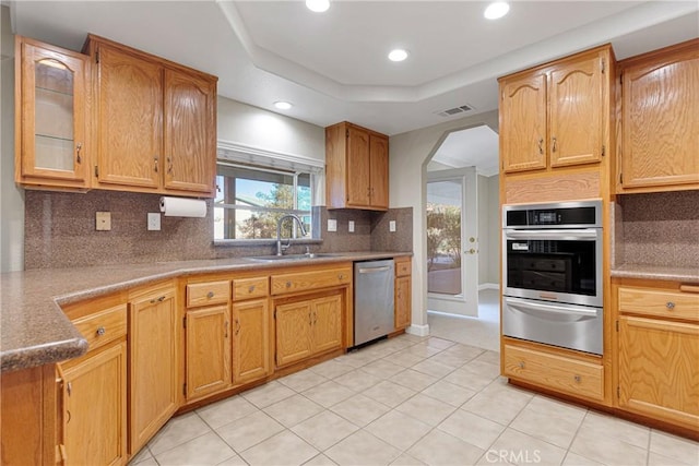 kitchen featuring sink, light tile patterned floors, appliances with stainless steel finishes, a raised ceiling, and backsplash