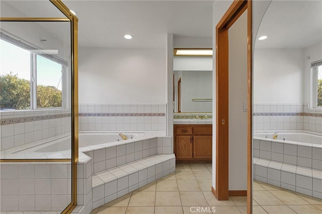 bathroom with tile patterned floors, tiled bath, vanity, and a wealth of natural light