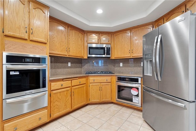 kitchen featuring decorative backsplash, stainless steel appliances, a raised ceiling, and light tile patterned flooring