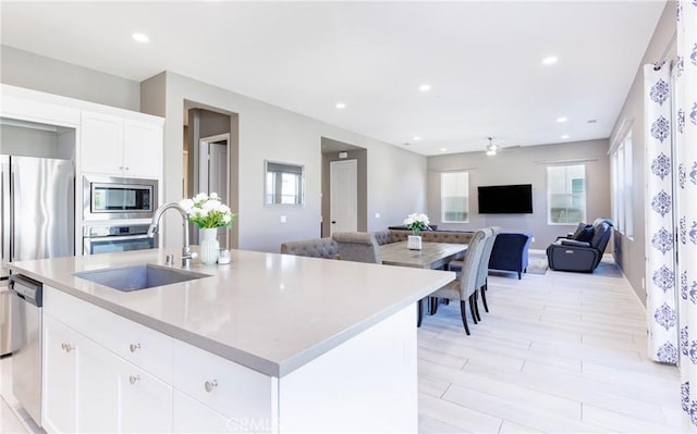 kitchen with sink, white cabinetry, a center island with sink, light wood-type flooring, and appliances with stainless steel finishes