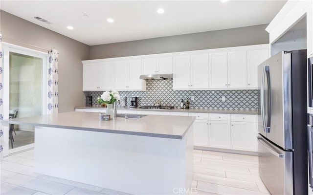 kitchen with appliances with stainless steel finishes, white cabinetry, sink, backsplash, and a kitchen island with sink