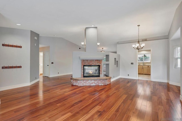 unfurnished living room featuring hardwood / wood-style flooring, a fireplace, vaulted ceiling, and a notable chandelier