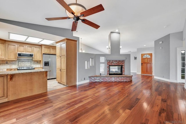 kitchen with backsplash, stainless steel appliances, light stone counters, a fireplace, and vaulted ceiling