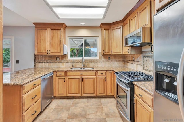 kitchen with stainless steel appliances, sink, light stone counters, and kitchen peninsula