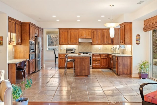 kitchen featuring sink, a breakfast bar area, appliances with stainless steel finishes, hanging light fixtures, and a kitchen island