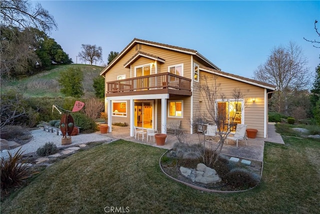 back of house with a balcony, a patio area, and a lawn