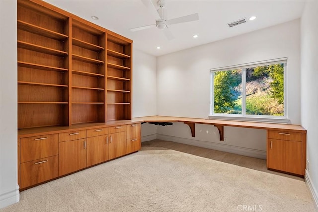 unfurnished office featuring built in desk, light colored carpet, and ceiling fan