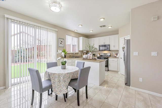 kitchen featuring sink, white cabinetry, light tile patterned floors, appliances with stainless steel finishes, and a kitchen island