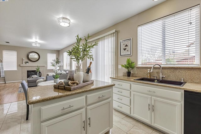 kitchen featuring black dishwasher, sink, a fireplace, and plenty of natural light