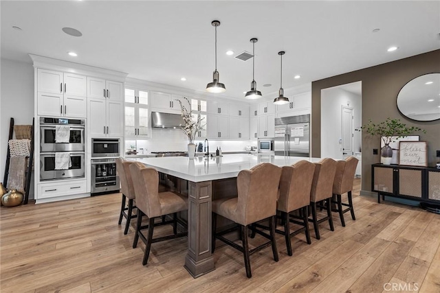 kitchen with a spacious island, a kitchen bar, built in appliances, pendant lighting, and white cabinets