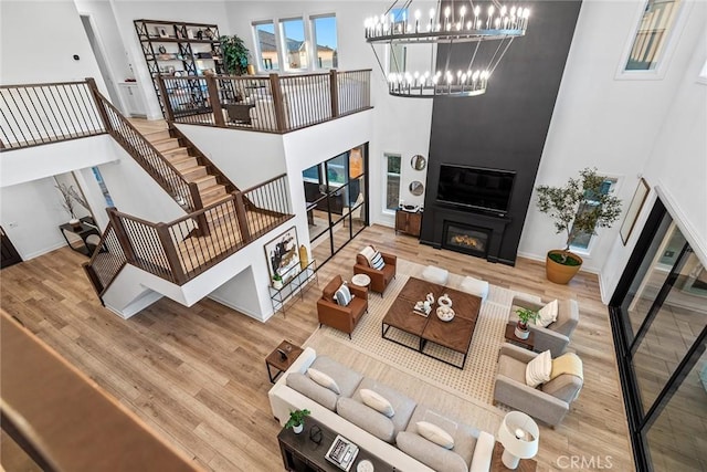 living room with hardwood / wood-style flooring, a large fireplace, a notable chandelier, and a towering ceiling