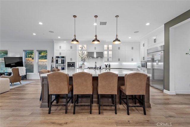 kitchen featuring a large island, a breakfast bar, built in appliances, extractor fan, and decorative light fixtures