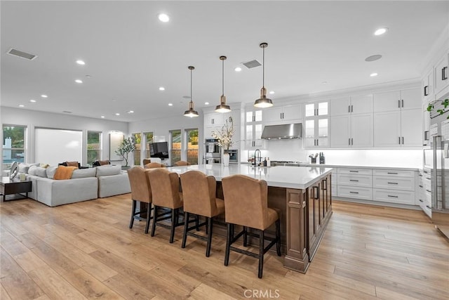 kitchen with ventilation hood, white cabinetry, a kitchen breakfast bar, hanging light fixtures, and a spacious island