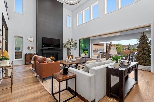 living room featuring an inviting chandelier, a towering ceiling, a fireplace, and light hardwood / wood-style flooring