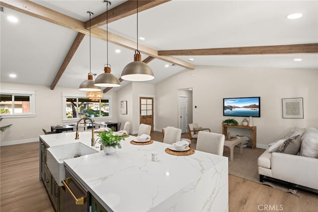 kitchen with light stone counters, decorative light fixtures, lofted ceiling with beams, a kitchen island with sink, and light hardwood / wood-style floors