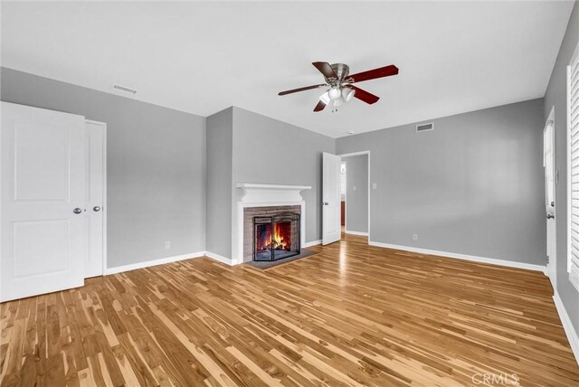 unfurnished living room featuring a warm lit fireplace, baseboards, visible vents, and light wood finished floors