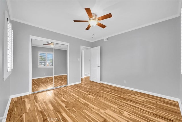 unfurnished bedroom with baseboards, a ceiling fan, ornamental molding, light wood-style floors, and a closet