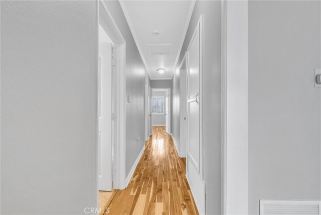 hallway with visible vents, baseboards, light wood-style floors, ornamental molding, and attic access