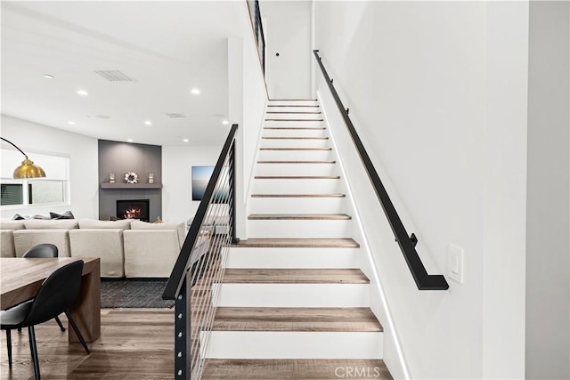 stairs featuring a large fireplace and wood-type flooring