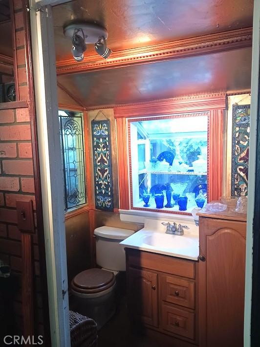 bathroom featuring vanity, ornamental molding, toilet, and brick wall