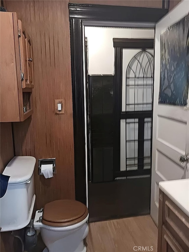 bathroom featuring hardwood / wood-style flooring, wooden walls, vanity, and toilet