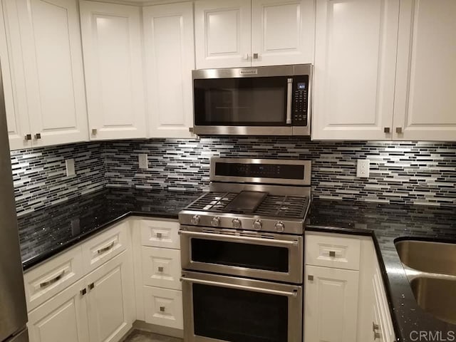 kitchen featuring sink, dark stone countertops, appliances with stainless steel finishes, white cabinets, and backsplash