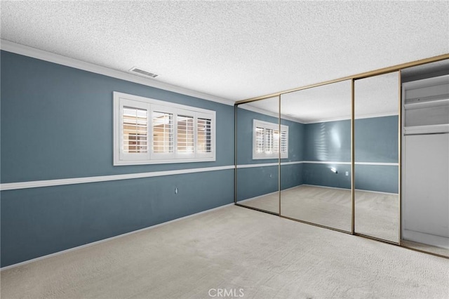 unfurnished bedroom featuring crown molding, a closet, visible vents, carpet flooring, and a textured ceiling