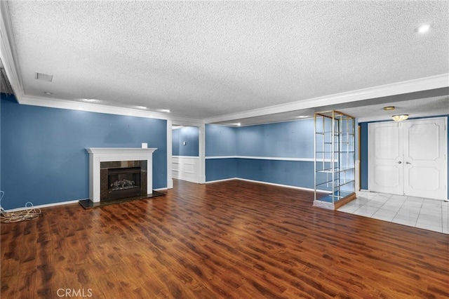 unfurnished living room featuring a textured ceiling, visible vents, a fireplace with raised hearth, and wood finished floors