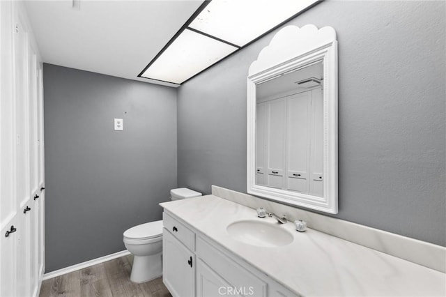 bathroom with a skylight, toilet, vanity, wood finished floors, and baseboards